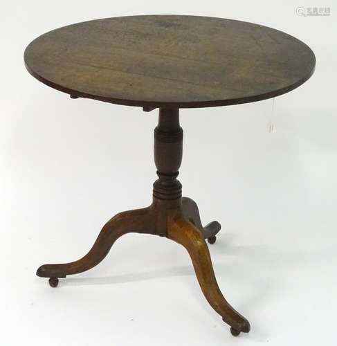 A Georgian oak tilt top table with a circular top above a tapering turned stem and a tripod base