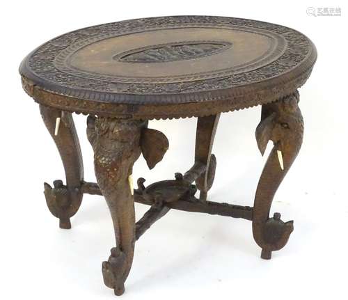 An early 20thC Anglo Indian table with an oval carved table top above four elephant formed supports