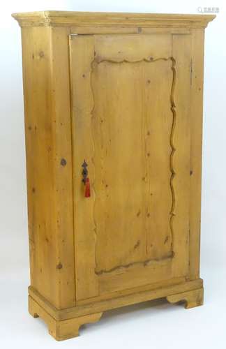 A 20thC pine cupboard with a moulded cornice above carved panelled door and shaped bracket feet.