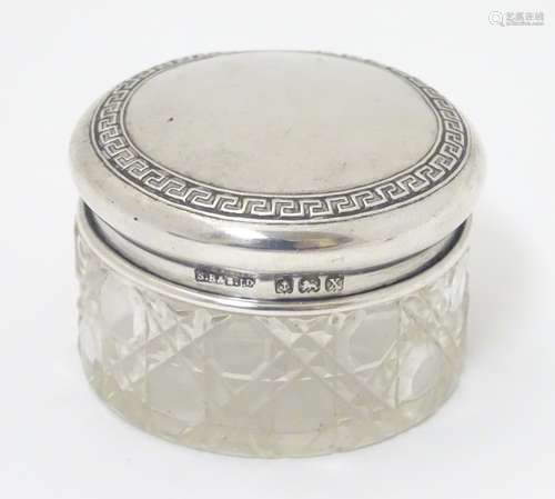 A cut glass dressing table pot with silver lid, having banded Greek key decoration.