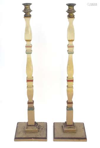 A pair of 20thC tall squared based candlesticks of carved wooden form with painted decoration and