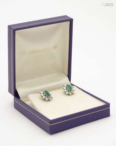 A pair of 9ct white gold stud earrings set with central emerald bordered by diamonds in a cluster
