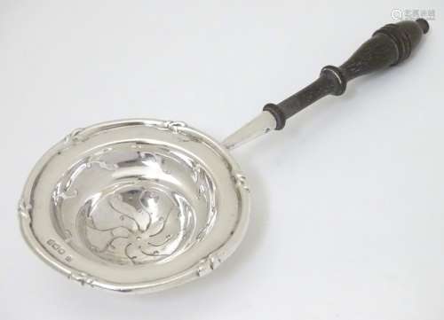 A silver tea strainer with turned wooden handle.