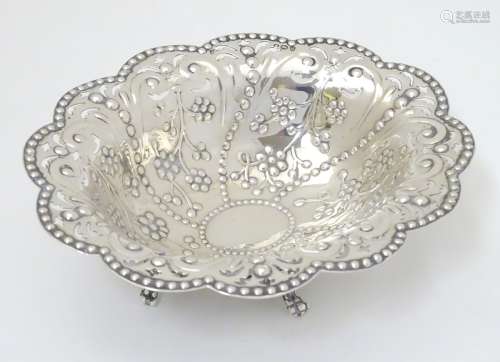 A silver dish with punch, pierced and embossed decoration and standing on four feet.