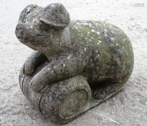 A 20thC reconstituted stone model of a pig resting on a barrel,