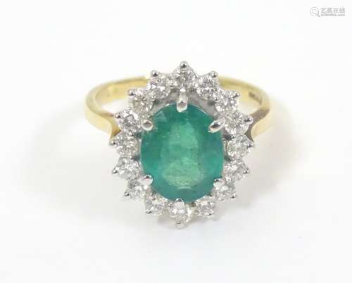 An 18ct gold ring set with central emerald bordered by diamonds. The setting approx ¾” x ½” overall.