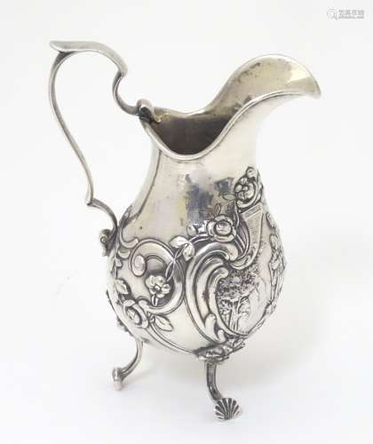 A Continental silver jug with floral and c-scroll decoration and central pictorial vignette.