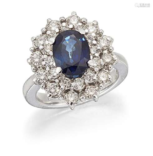 A sapphire and diamond cluster ring, the claw-set oval sapphire within a brilliant-cut diamond