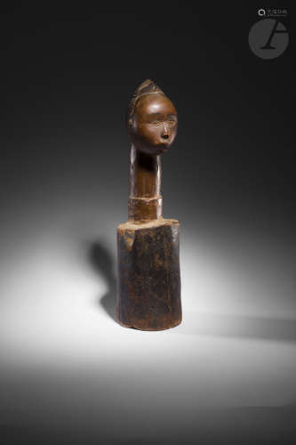 Une sculpture représentant une tête tressée sur un long cou surmontant un long cylindre, probable