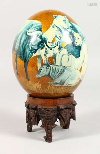 AN OSTRICH EGG DECORATED WITH AFRICAN ANIMALS, on a carved wood stand. 8.5ins high.