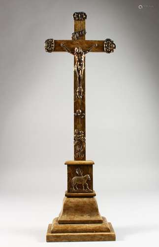 A WOODEN CRUCIFIX, with embossed white metal Corpus Christi and other emblems. 23ins high.