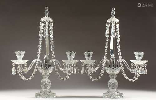 A PAIR OF GLASS TWO BRANCH CANDLESTICKS, with prism drops, on a circular base. 21ins high.