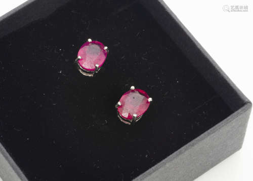 A pair of treated ruby ear studs, oval mixed cut in silver four claw setting, boxed