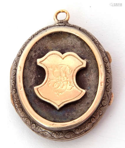 Antique silver oval locket, the front applied with a gold shield engraved with a monogram, the verso