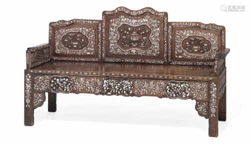 A Chinese carved hardwood and mother of pearl inlaid settle, the back formed of three panels carved with foliage, birds and Foo dogs. C. 1900.