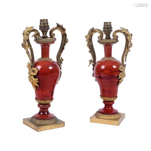 A pair of French gilt metal and red glazed ceramic urn table lamps