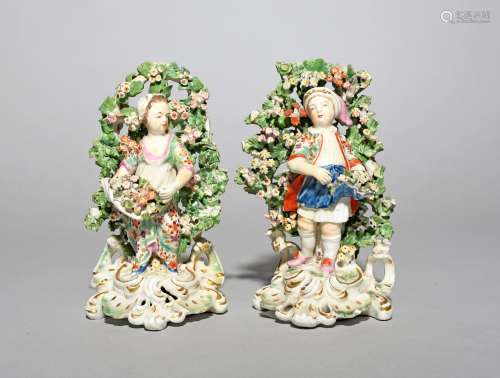 A pair of Derby figures of children, c.1770, each standing before tall flowering bocage with further