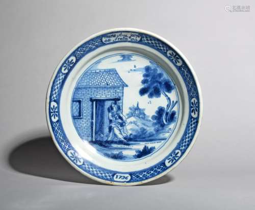 A large Delft dish, 18th century, painted in blue with a figure seated in the doorway of a low brick