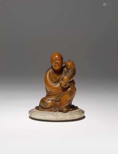 A CHINESE SOAPSTONE SEATED FIGURE QING DYNASTY OR LATER Carved as a luohan holding a small lion