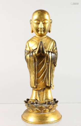 A CHINESE GILT BRONZE FIGURE, of a Buddha standing hands clasped, on a lotus pad. 9ins high.