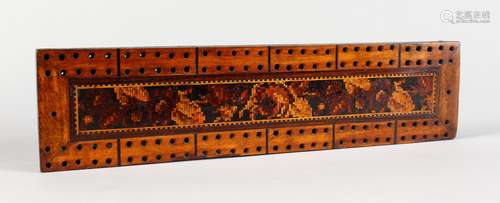 A TUNBRIDGE WARE MARQUETRY CRIBBAGE BOARD, on four ball feet. 9.25ins long x 2.25ins wide.