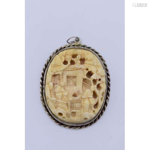 A Chinese carved ivory and white metal mounted oval pendant,