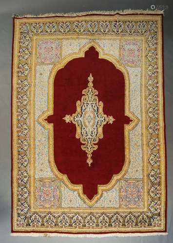 A large Iranian woolen ruby ground carpet, with central floral lozenge, within a cream border