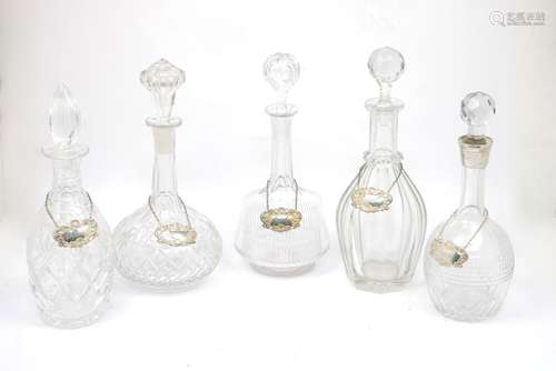 Five glass decanters, one with silver collar, and five silver labels200