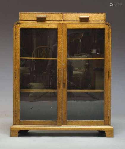 An Art Deco oak bookcase, the raised top with two frieze drawers, above two glazed cupboard doors,