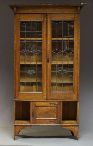 An Arts and Crafts oak bookcase, the moulded cornice above two leaded and stained glass doors,