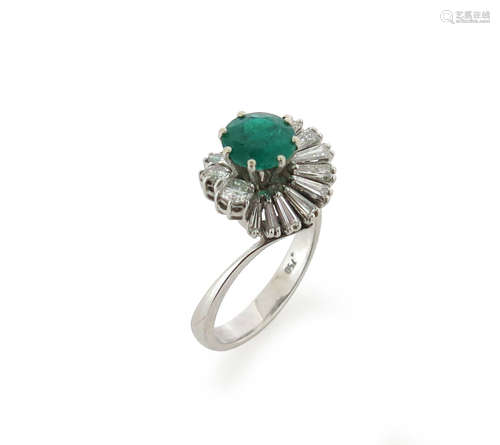 An emerald and diamond cluster ring, the circular-cut emerald is set within a surround of circular