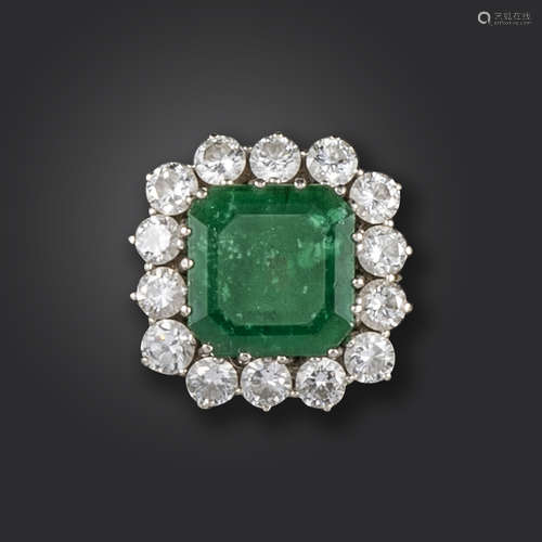 An emerald and diamond cluster ring, the emerald-cut emerald is set within a surround of round