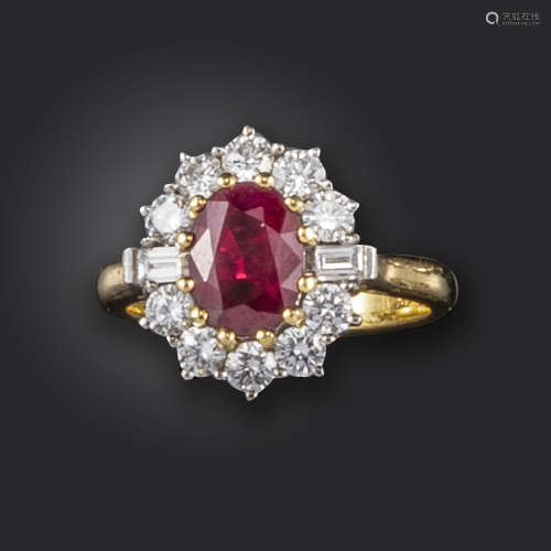 A ruby and diamond cluster ring, the oval-shaped ruby set within a surround of circular-cut and