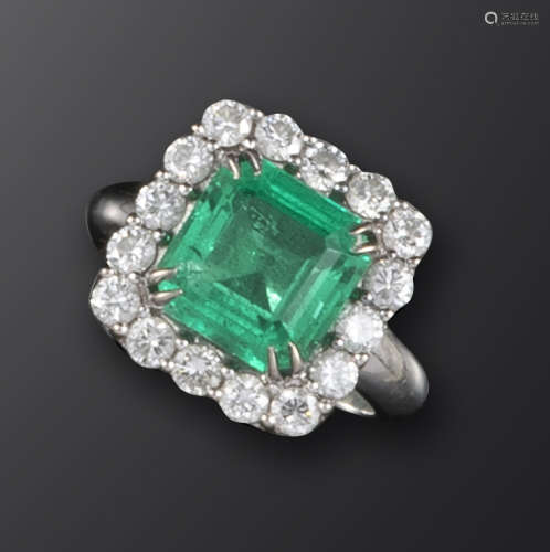 An emerald and diamond cluster ring, the emerald-cut emerald weighs approximately 2.95cts, set