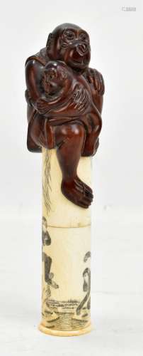 A Japanese bone scroll holder with applied mother and baby ape finial, the body decorated with