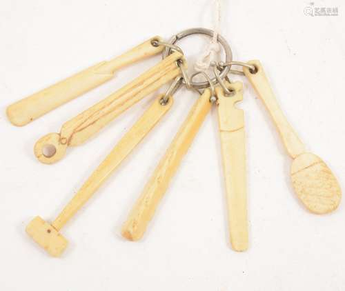 A carved bone teething ring, in the shape of carpenter’s tools, a club and a cricket bat, 9cm.