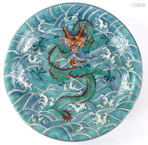 A doucai style circular dish, decorated with a coiled five-clawed dragon beside waves; the base with