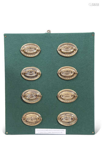 Set of eight embossed brass furniture handles mounted on a baized fronted wooden wall frame, label