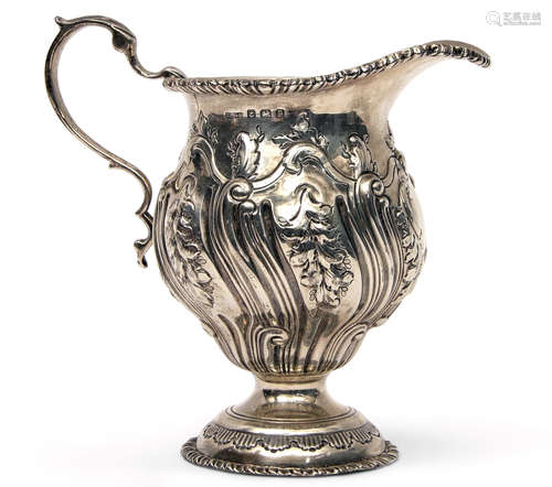 George V cream jug of circular baluster form in George II style, heavily chased and embossed with