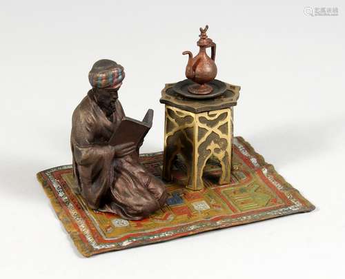 A COLD PAINTED BRONZE GROUP, ARAB READING A BOOK, on a carpet. 5.5ins long.