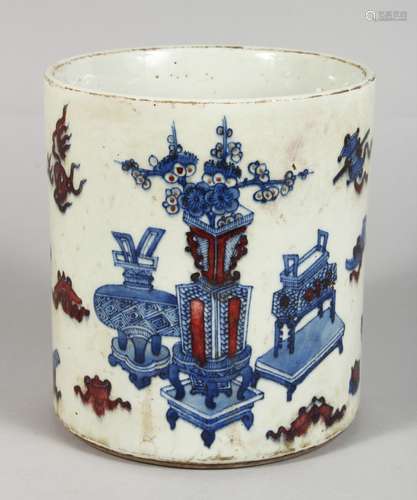 A CHINESE PORCEAIN BRUSH POT, painted in blue and red, with vases and other emblems. 7ins high.