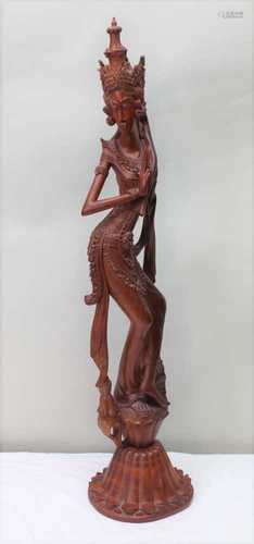 A 20TH CENTURY BALINESE CARVED WOOD GODDESS, in a sinuous dancing pose, wearing a crown, on lotus