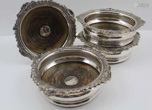 A SET OF FOUR GEORGIAN DESIGN SILVER-PLATED BOTTLE COASTERS, cast decorative rims, turned wood