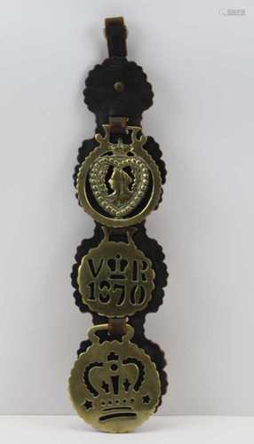 A LEATHER HARNESS STRAP OF THREE VICTORIAN HORSE BRASSES, Queen Victoria related, the top one has