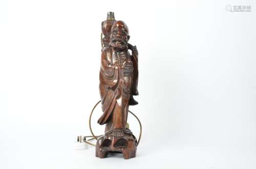 A hardwood Chinese lamp, in the form of an Immortal holding a staff and peach, height excluding