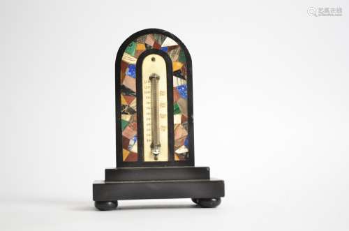 A pietra dura desk thermometer, of arched form with a profusion of inlaid coloured stones, raised on