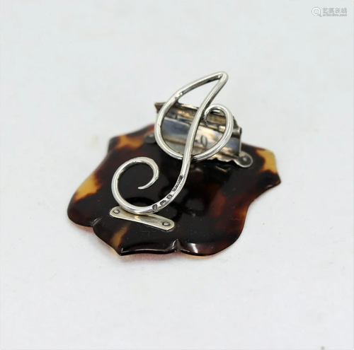 A silver treble clef paper clip mounted on a tort…