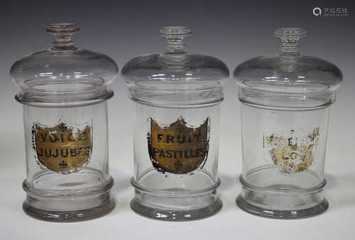 Three clear glass storage jars and covers with original labels, late 19th century, the first