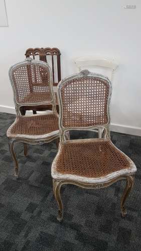A pair of continental painted and caned back single chairs, the distressed paintwork to the carved