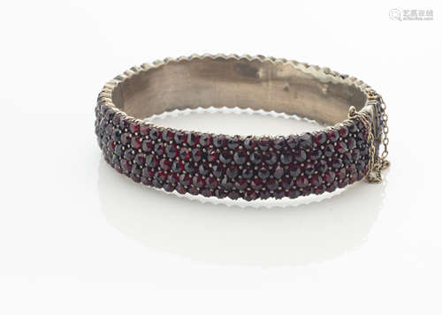 A 19th Century garnet bangle, the hinged bangle encrusted with rose cut garnets marked to tongue